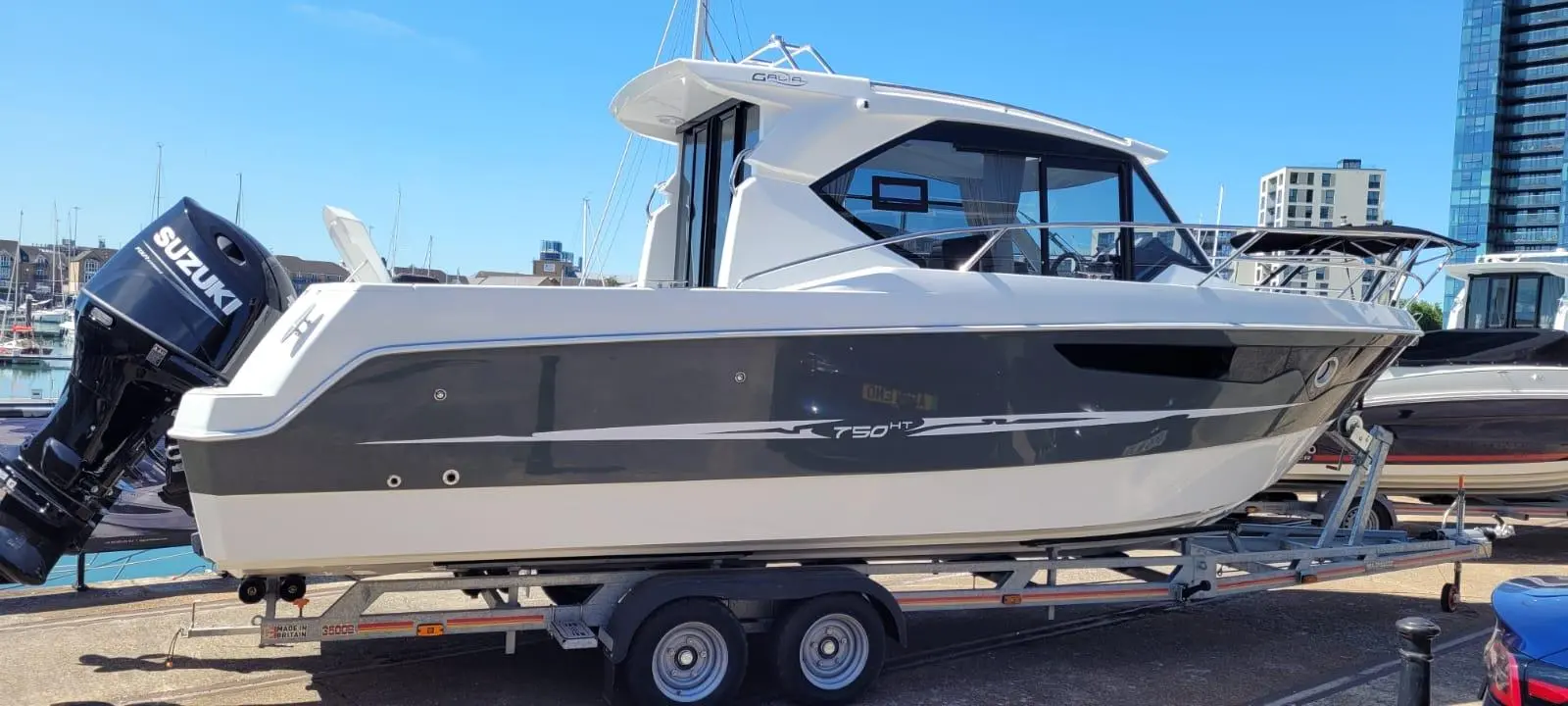 A white and grey boat, model T50 HT, on a trailer in a marina, with a Suzuki outboard motor visible.
